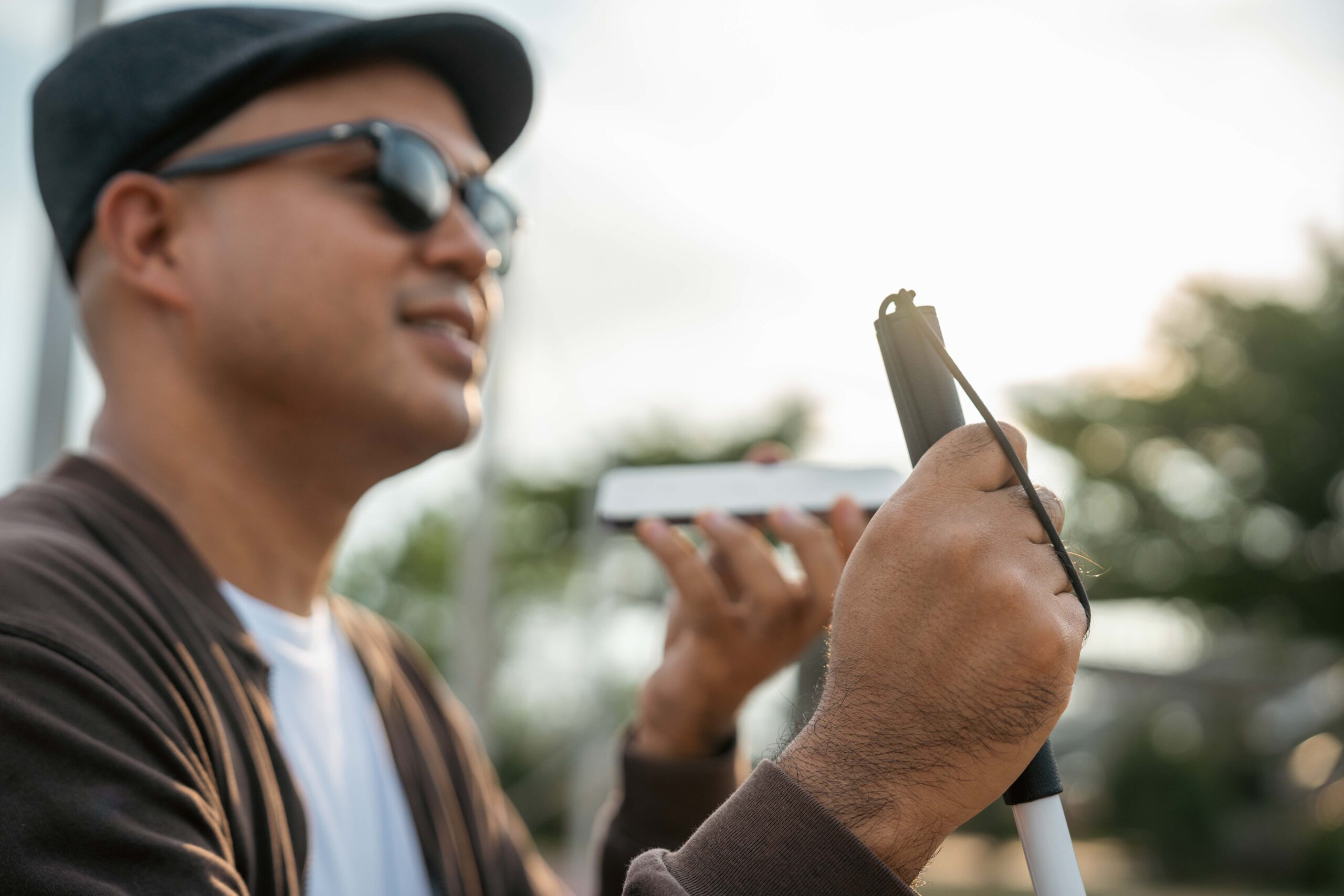 Junger asiatischer blinder Mann, der eine Anwendung auf seinem Mobiltelefon benutzt, die Menschen mit Sehbehinderung den Zugang erleichtert. Technologie für blinde Menschen, um Sprachnachrichten zu senden oder für Navigation.